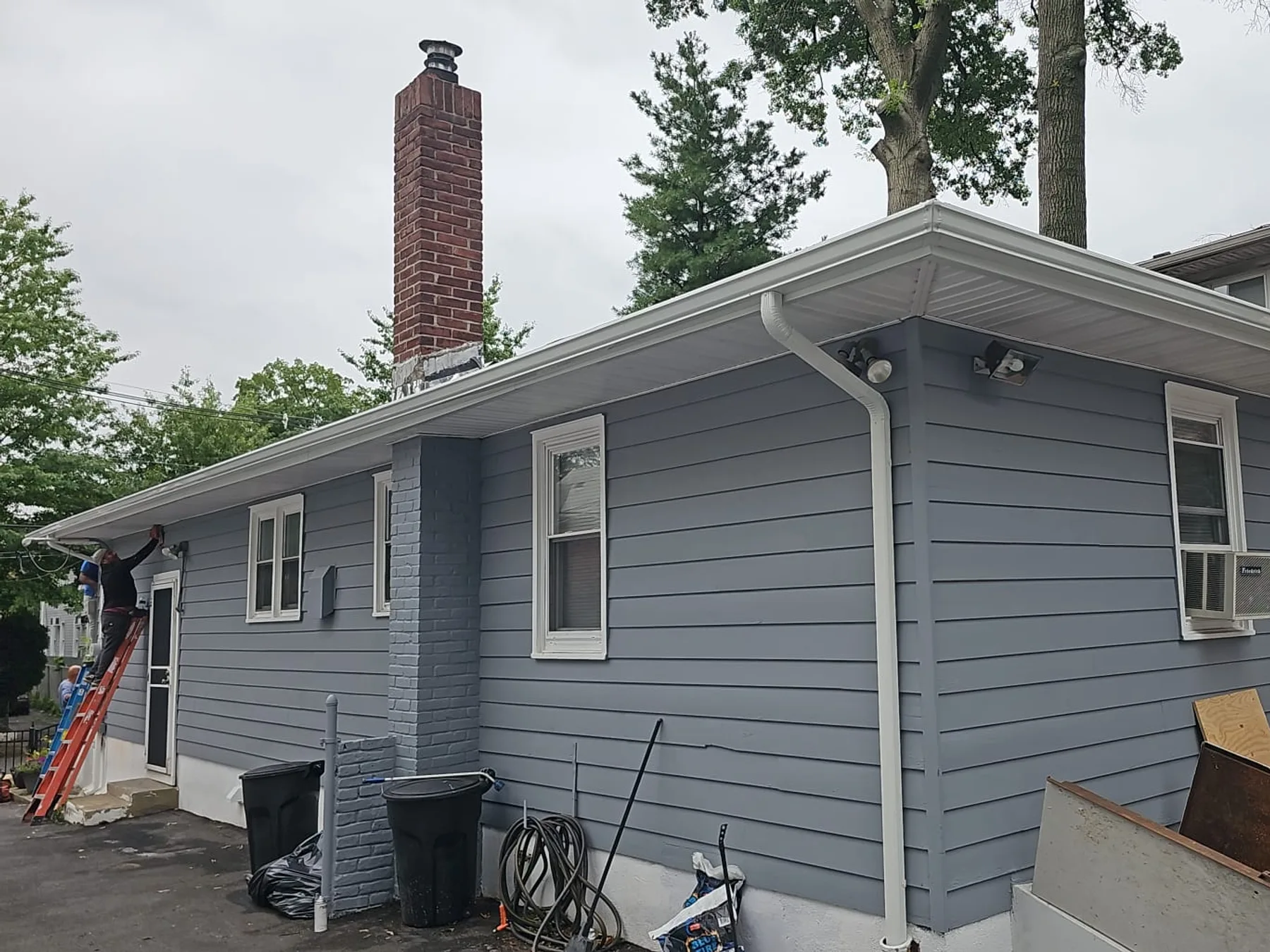 AJ Gutters LLC technician installing gutters on a ladder at a blue-gray home