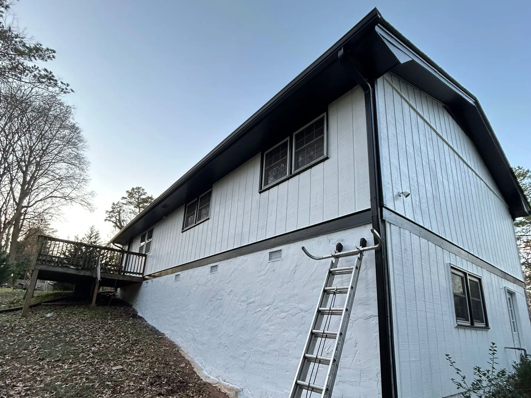 Ladder set against a two-story home for gutter work at dusk